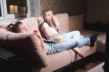 一对年轻迷人的长发情侣在家里独自拥抱在沙发上看电视。在流感大流行期间与亲人共度时光的概念