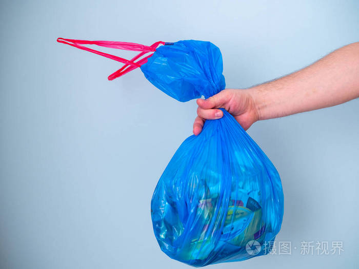 男人手拿着蓝色塑料垃圾袋隔离在蓝色背景上