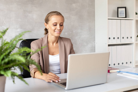 微笑的女人坐在办公室里看着笔记本电脑屏幕