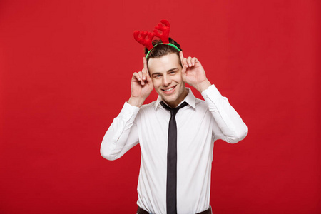 圣诞概念帅气的商务男士庆祝圣诞快乐，新年快乐戴着驯鹿发带，举着兔子的手势。