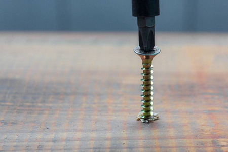 老年的木板表面用螺丝刀把金属螺钉拧进木板表面.