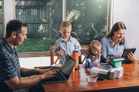 在家工作和家庭教育的概念。父母和两个儿子坐在桌子旁。