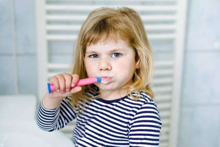 可爱的小女孩手里拿着牙刷，一边刷牙一边微笑。有趣快乐健康的孩子学习早晨洗脸和刷牙路线