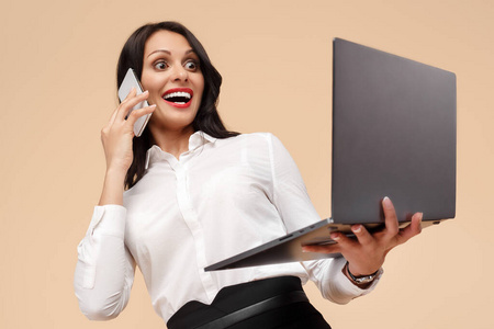 一位年轻的现代商务女性拿着米色背景的笔记本电脑在智能手机上聊天。