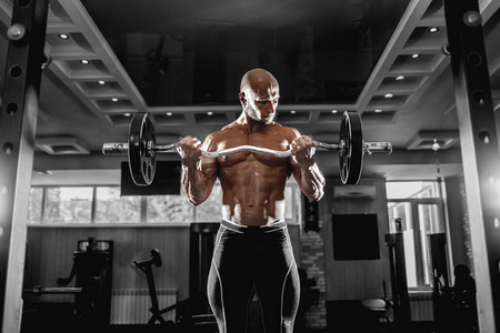 肌肉发达的男子在健身房锻炼，肱二头肌上有哑铃，强壮的男性躯干腹肌