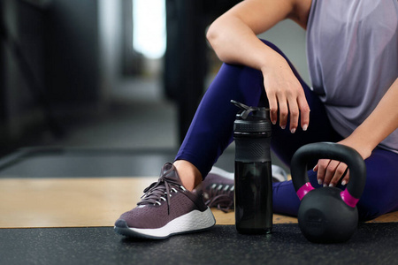 体育运动的概念。健身器材。一个穿着运动鞋的女人坐在地板上。一个壶铃和一个哑铃。