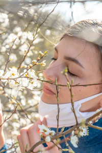 特写镜头在一棵开满鲜花的杏树下，一个戴着冠状病毒面具的女孩闭着眼睛。