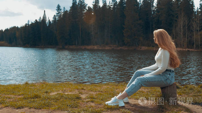 美丽的年轻金发女人坐在湖边的公园里放松侧视图