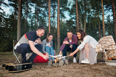 一群朋友在森林营地放松.男人和女人在篝火上准备棉花糖.