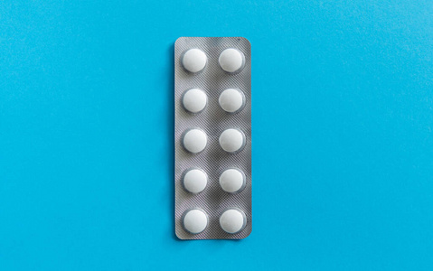 包里药片的俯视图。蓝色背景的白色药丸。药品，药物，止痛药，片剂，药物，抗生素，维生素，治疗，胶囊，剂量。药房主题。