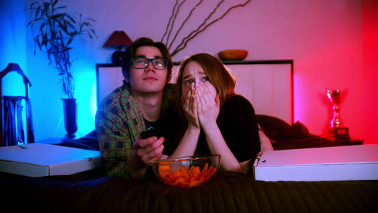 年轻漂亮的情侣躺在床上看恐怖电影-女朋友害怕了照片