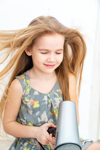 little girl drying her long hair with hair dryer 