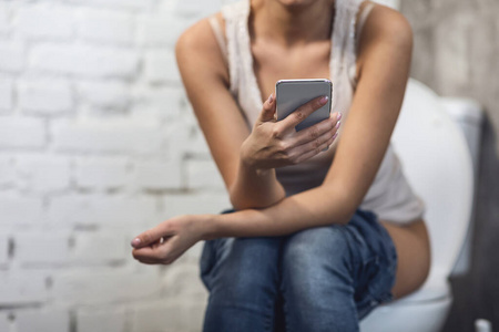 坐在洗手间马桶上的不认识的用手机的女孩照片