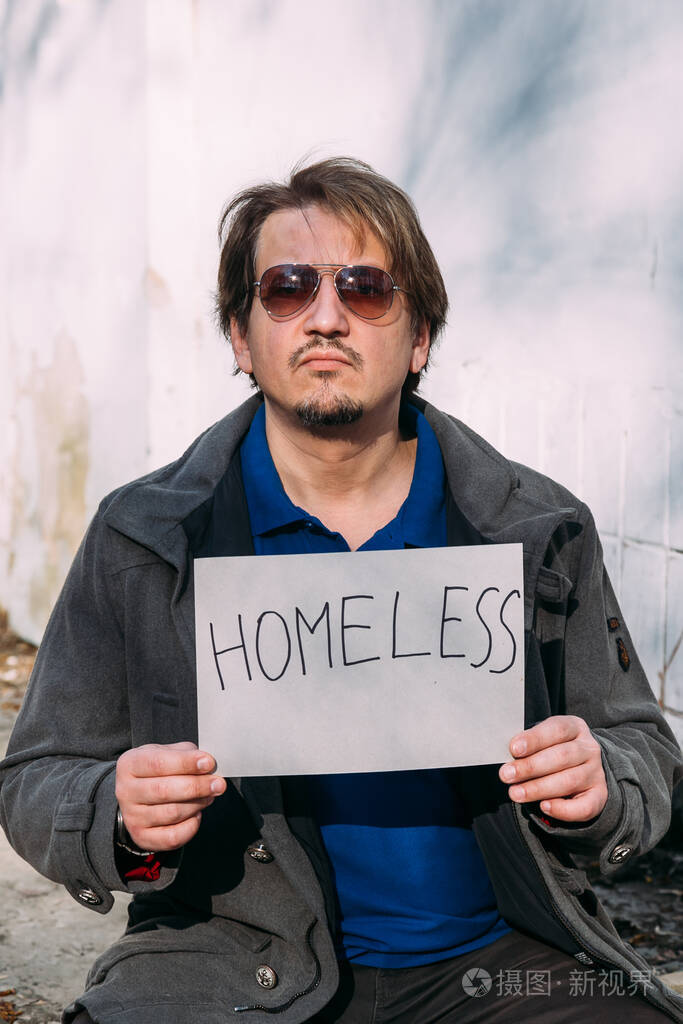 可怜的人坐在垃圾堆上拿着一块写着无家可归者的纸板