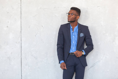 一个自信的年轻非洲商人在灰色的水泥墙上摆出一副现代西装和蓝色衬衫的样子