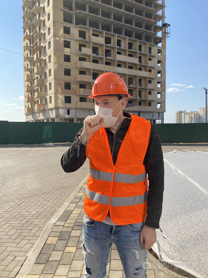男建筑工人穿着工作服戴着医用口罩在建房屋背景下咳嗽感染威胁的概念