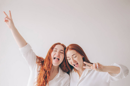两个红头发的姐妹穿着宽大的衬衫，孤立地站在白色的背景上。两个年轻女人在镜头前鬼混。他们做鬼脸玩得很开心