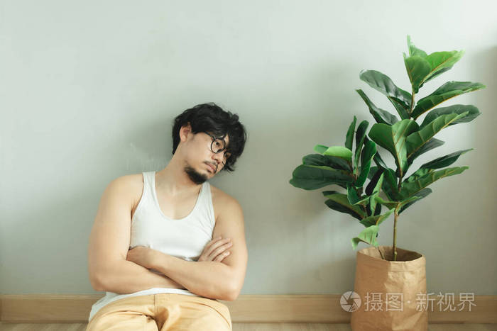 寂寞无聊的男人绝望地坐在地板上房间里有盆栽植物