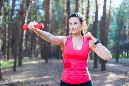 运动型迷人的女孩用哑铃锻炼，在森林里训练。健身运动生活方式理念