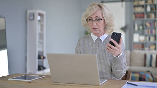 一位老妇人在用智能手机和笔记本电脑工作