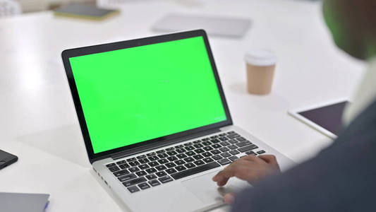 一个非洲男人在用绿色彩色键控屏幕的笔记本电脑工作