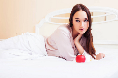 年轻漂亮的黑发女人躺在床上，豪华的白色室内复古早餐可爱
