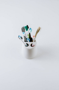 Different types of toothbrushes in a white cup. 