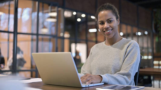 一名非洲妇女在操作笔记本电脑时对着摄像机微笑