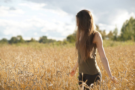 Elegant woman with long hair standing waistdeep in wheat field 
