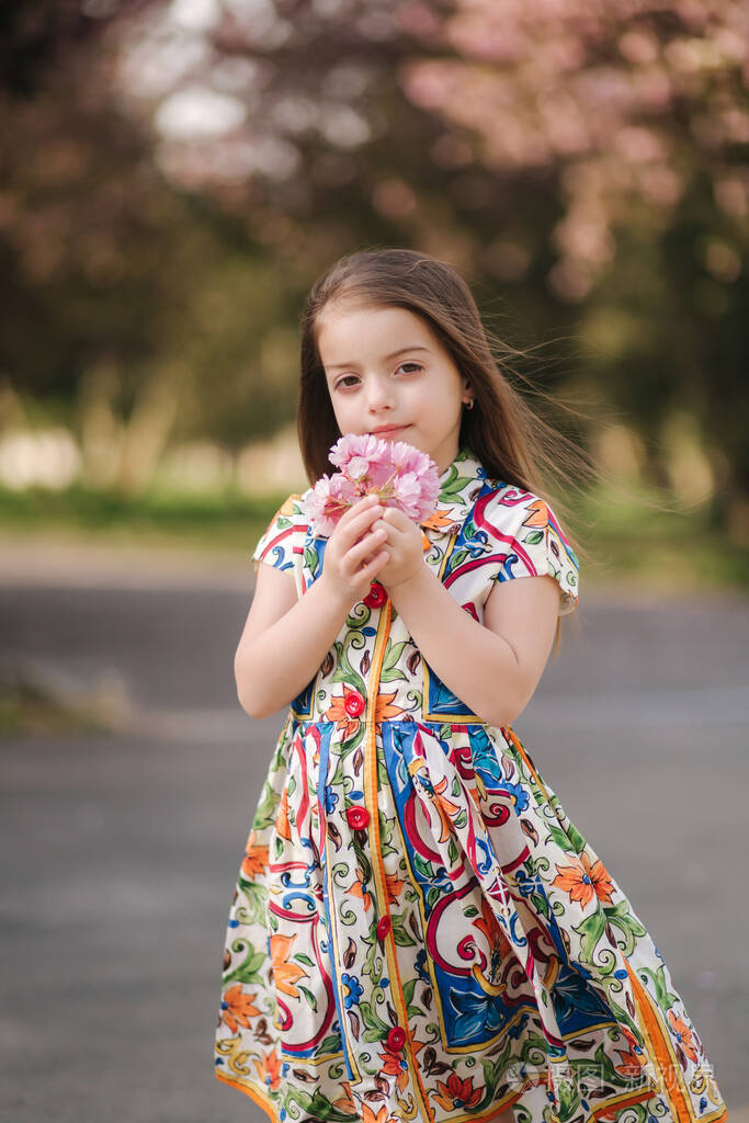 可爱的小女孩穿着漂亮的衣服手里拿着花公园里的樱花树女童装模特