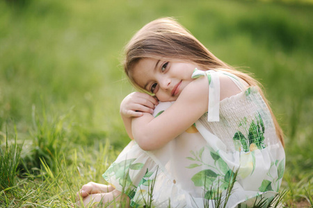可爱的小女孩赤脚坐在公园的草地上。新鲜空气中的快乐孩子