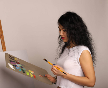 画架上的画家画了一幅画。漂亮的女孩用刷子画画。一张新画的空白画布和一个拿着画笔和颜料的艺术家。