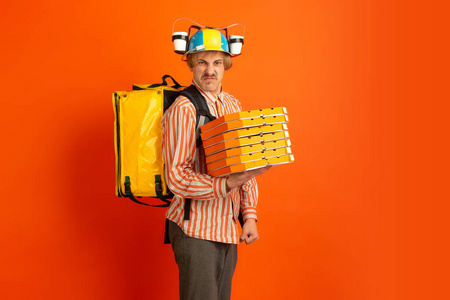 检疫期间的无接触送货服务。绝缘期间，男子运送食物和购物袋。在橙色背景下孤立的送货员的情绪。
