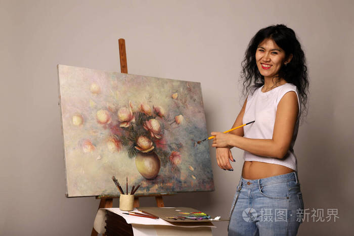画架上的画家画了一幅画漂亮的女孩用刷子画画油画画布上花瓶里的玫瑰