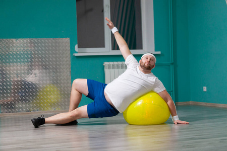 健身的胖子微笑的胖子正在用健身球做运动.