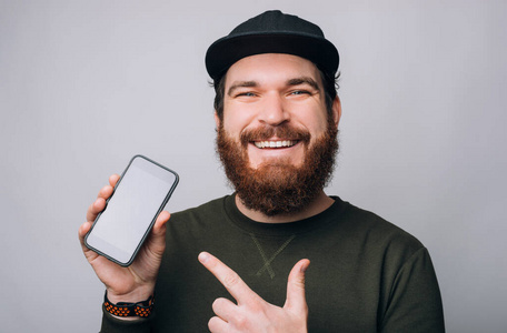 一个快乐的大胡子男人指着他拿在白色背景上的手机。