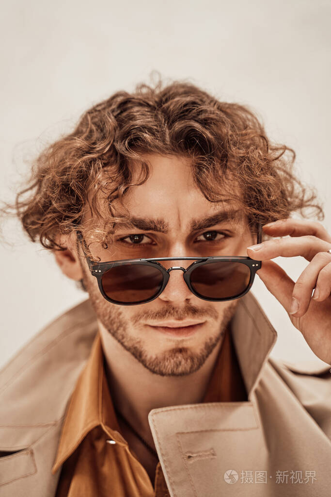 一个留着卷发的帅哥在明亮的工作室里摆姿势摘下眼镜