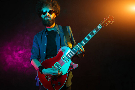 一个头发卷曲的时髦男人，霓虹灯下的红色吉他。摇滚音乐家正在弹电吉他。