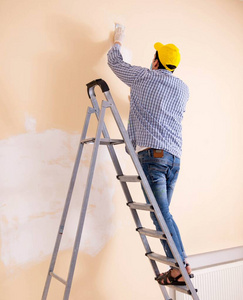 年轻的承包商用砂纸打磨墙壁照片