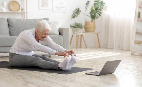 活跃的老年妇女在笔记本电脑前做热身伸展运动