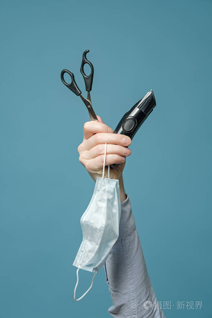 男性手拿剪刀修剪器和医用面罩隔离的概念和不能去理发店垂直照片