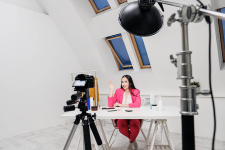 一位女性美女博主在一间白屋子里录制一段视频。三脚架上的照明和相机。