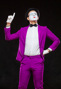 男哑剧演员的肖像，孤立在黑色背景上。穿着紫色西装的年轻人竖起手指站着。注意警告非好处的象征