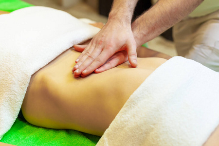 手按摩女性腹部侧视图。治疗师对腹部施压。在spa沙龙接受按摩的女士