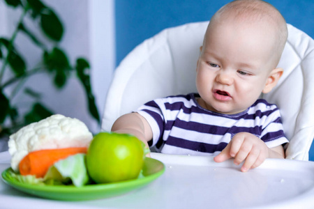 婴儿食品。一个不高兴的白人小孩把盘子从自己的高脚椅上推开。新鲜蔬菜和水果。新生婴儿