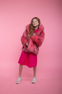 女孩时装模特穿着时髦的衣服，浅粉色的皮草外套在工作室的粉色背景上。风格。
