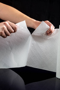 Hands tear off a piece of white paper towel from a roll on a bla