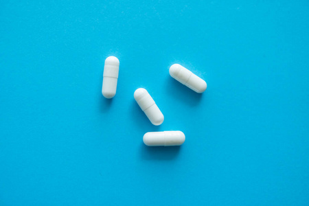 蓝色背景的白色药丸。药品，药物，止痛药，片剂，药物，药物，抗生素，维生素，治疗。药房主题。蓝色表面散落的药丸的俯视图。