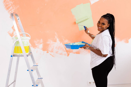 美丽的非洲裔美国女孩用油漆辊在墙上作画。一个年轻漂亮女人在她的新公寓里粉刷墙壁的肖像。重新装修和翻新概念。
