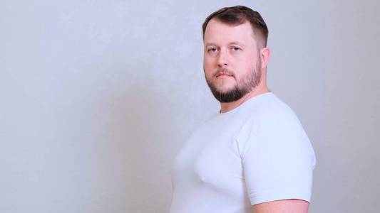 特写写真一个白人大胖子,绿眼睛直视镜头,身穿白色t恤,表情怀疑可疑